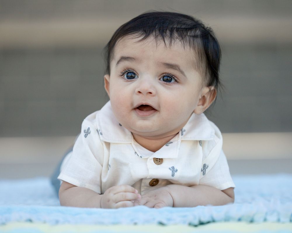 Baby wearing white polo shirt lying on blue blanket looking upward with curious expression.