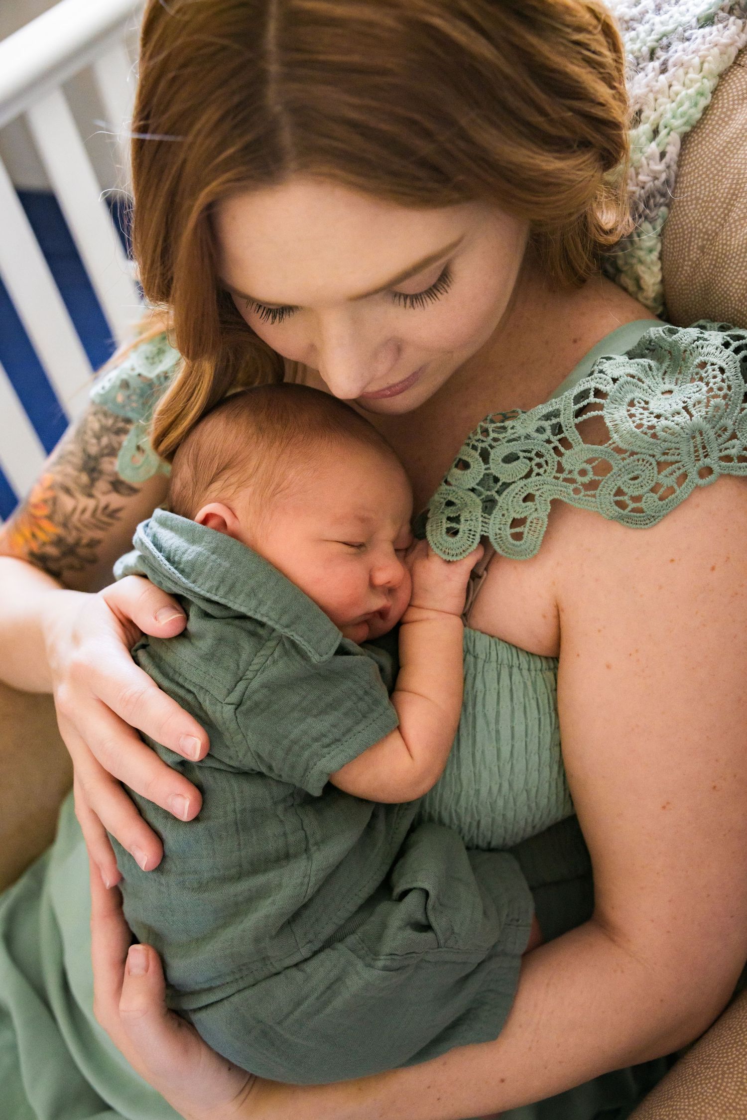 A baby in a green outfit sleeps peacefully while being held in a tender embrace.