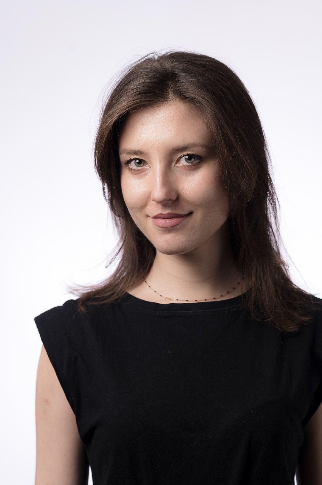 Professional headshot portrait of a person with brown hair and a black sleeveless top against a light background.
