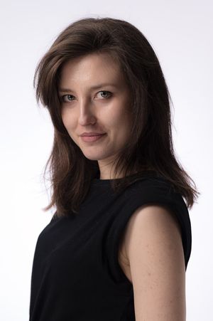 Professional studio portrait with dark brown hair wearing a sleeveless black top against light background.