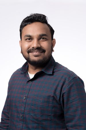 Professional headshot of someone wearing a plaid button-down shirt against a light background, smiling warmly at the camera.