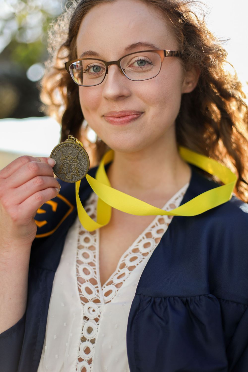 Graduate in navy gown shows off their graduation medal during outdoor photo session.
