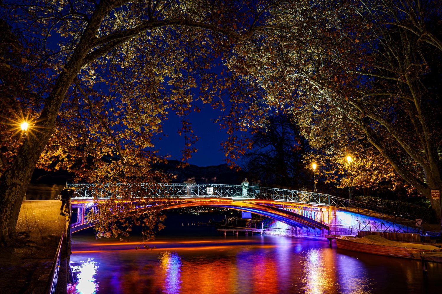 Illuminated bridge over water with colorful lights reflecting in the river at night.
