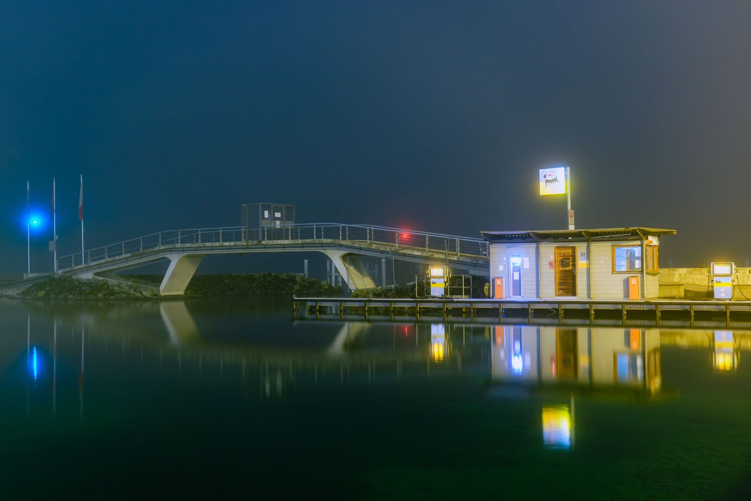 Illuminated buildings and structures reflect on calm water at night creating a serene mirror-like panorama.
