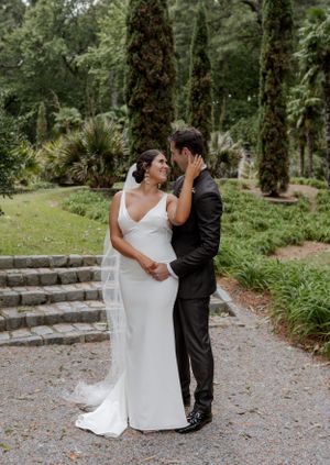 A tender wedding moment captured in a lush garden setting with stone steps and cypress trees.