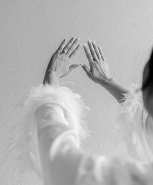 Silhouette of a bride adjusting her veil by a window with natural light streaming in.