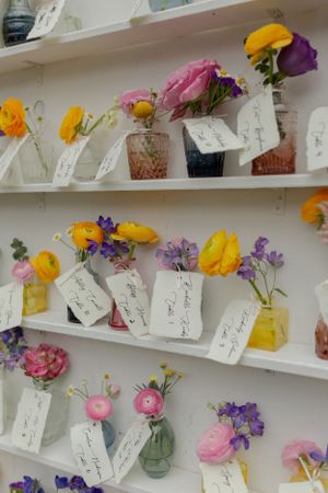 Colorful flower arrangements in small vases on white shelves with handwritten name cards.