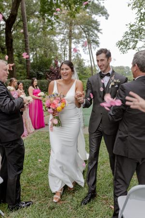 Joyful wedding celebration with pink flower petals falling in an outdoor garden setting.