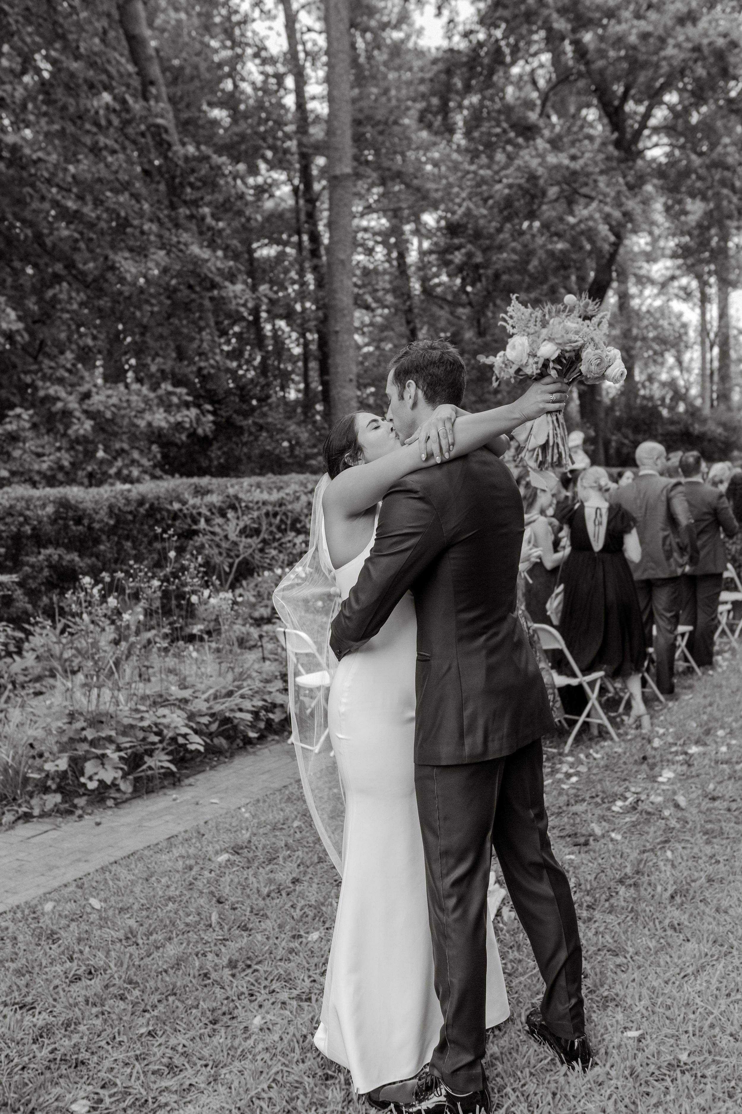 Black and white photo of newlyweds embracing during outdoor wedding ceremony.