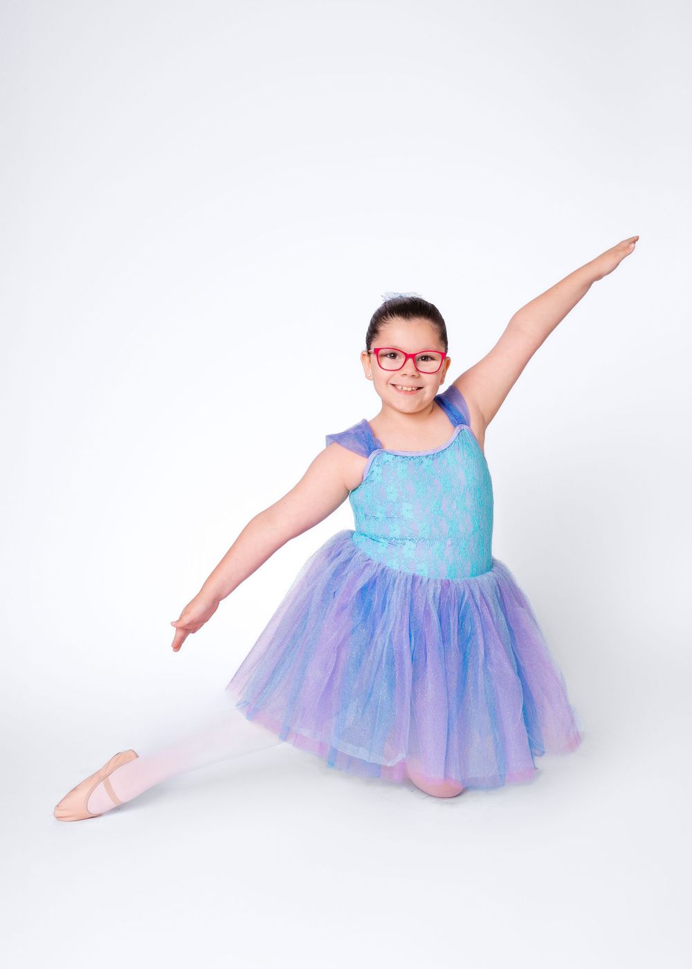 Dancer in sparkly blue and purple tutu striking graceful pose against white background.