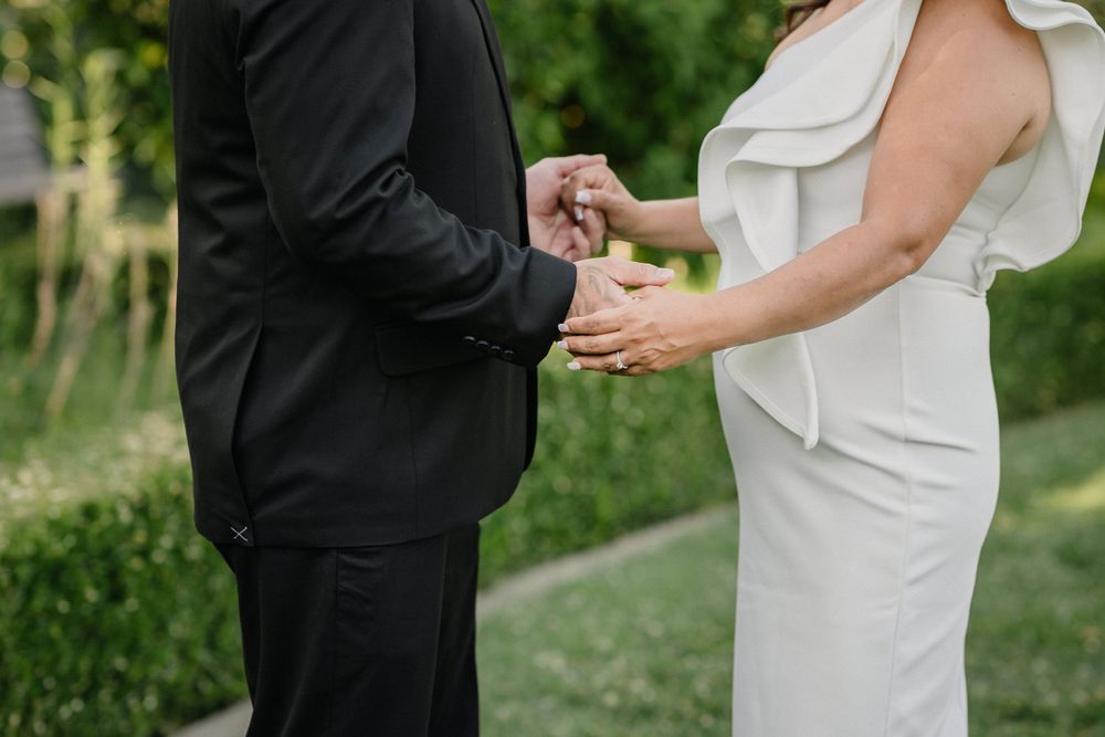 Close-up of couple's hands exchanging rings during an outdoor garden wedding ceremony.