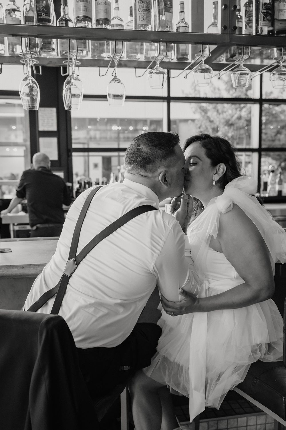 Couple in formal attire sharing a tender moment at an elegant bar setting captured in monochrome.
