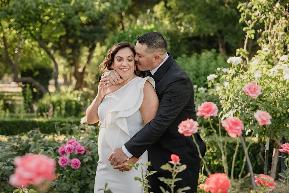 Romantic moment between newlyweds in a blooming rose garden during golden hour.