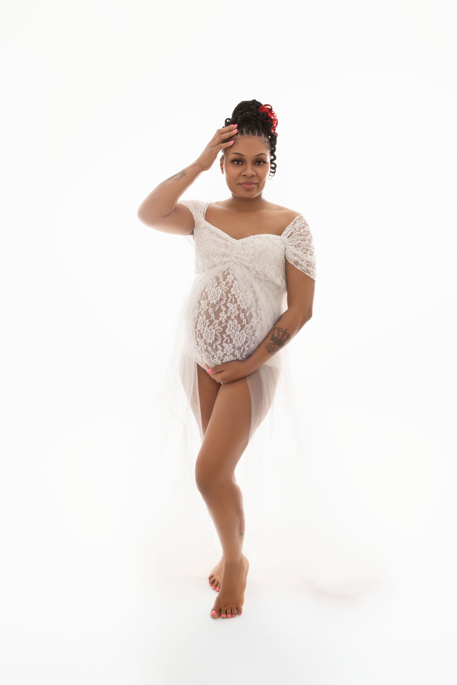 An expected mother poses for the camera in a high key white studio wearing a white lace bodysuit in Cedar Park, TX.