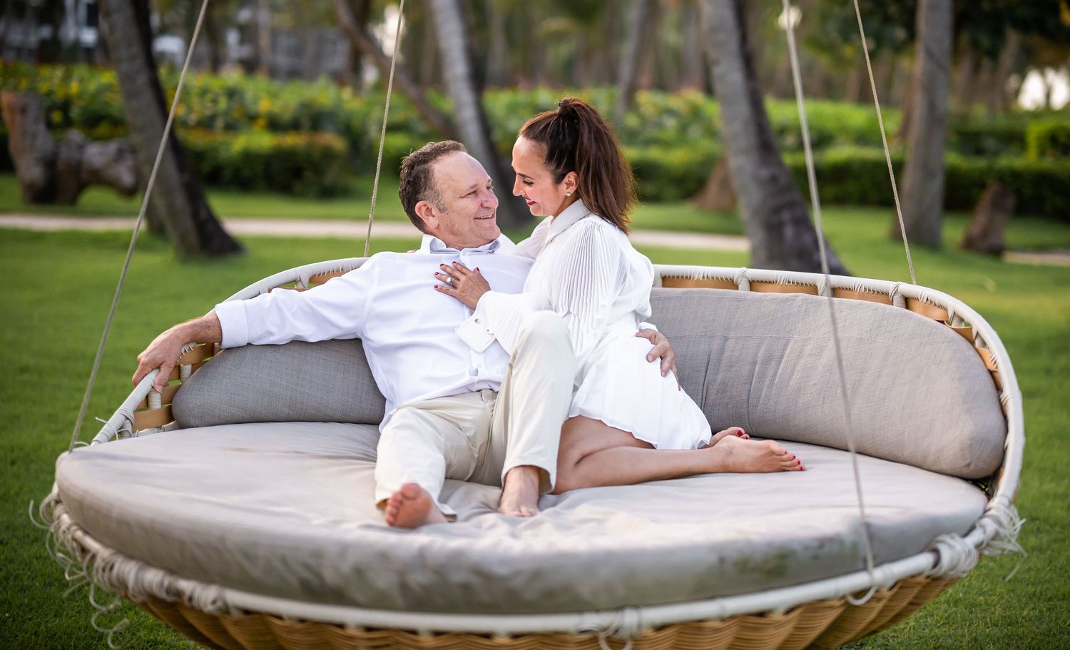 Couple lounging together on a large outdoor hanging daybed surrounded by greenery.