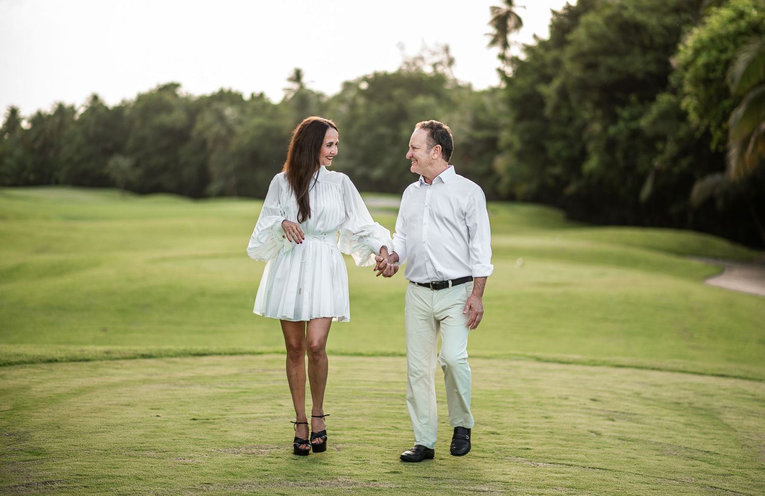 A couple strolls together on a lush green golf course.