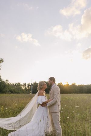 A romantic wedding couple embraces in a sun-drenched meadow during sunset.