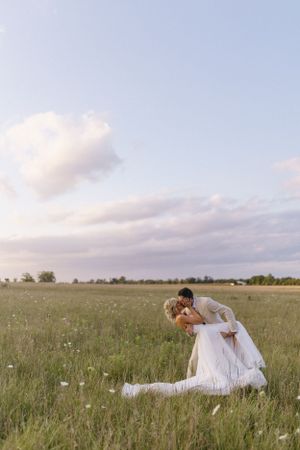 A romantic dip pose captured in a serene meadow under soft clouds.
