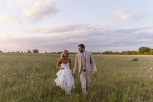 Newlyweds walking together through a wildflower meadow at dusk.