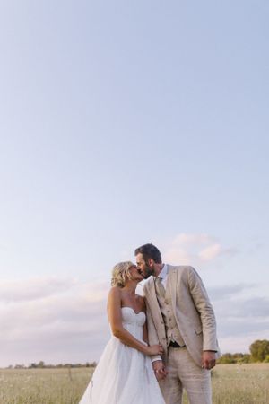 Intimate wedding portrait in a sunset meadow with soft clouds overhead.