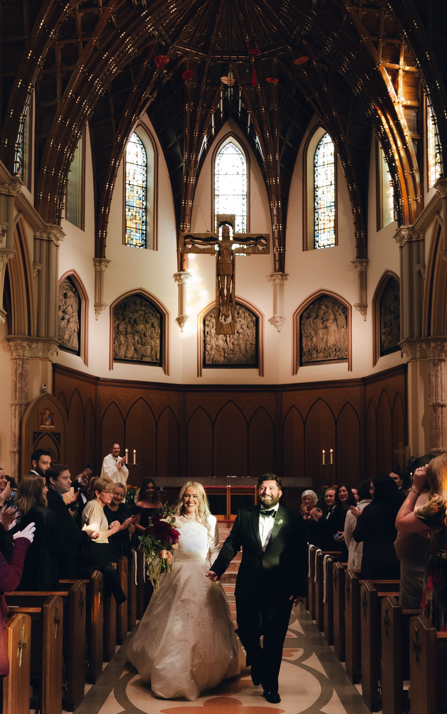 A couple stands beneath a gothic archway overlooking a courtyard with ornate architecture and climbing vines.