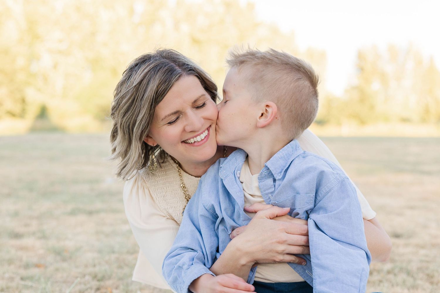 Loving mother smiling as her young son gives her a sweet kiss on the cheek outdoors.