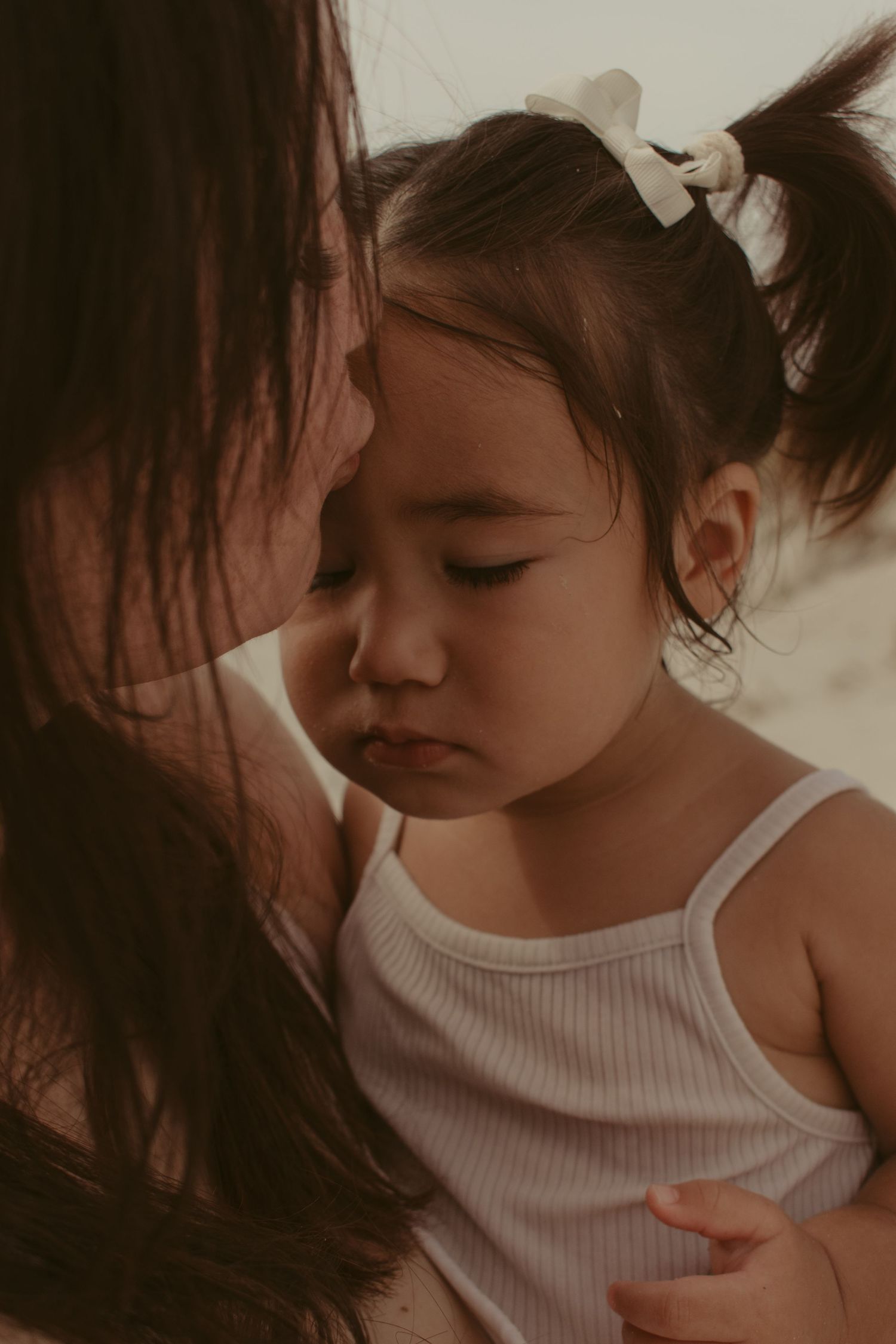 Intimate mother-child bonding moment captured in soft, moody lighting.