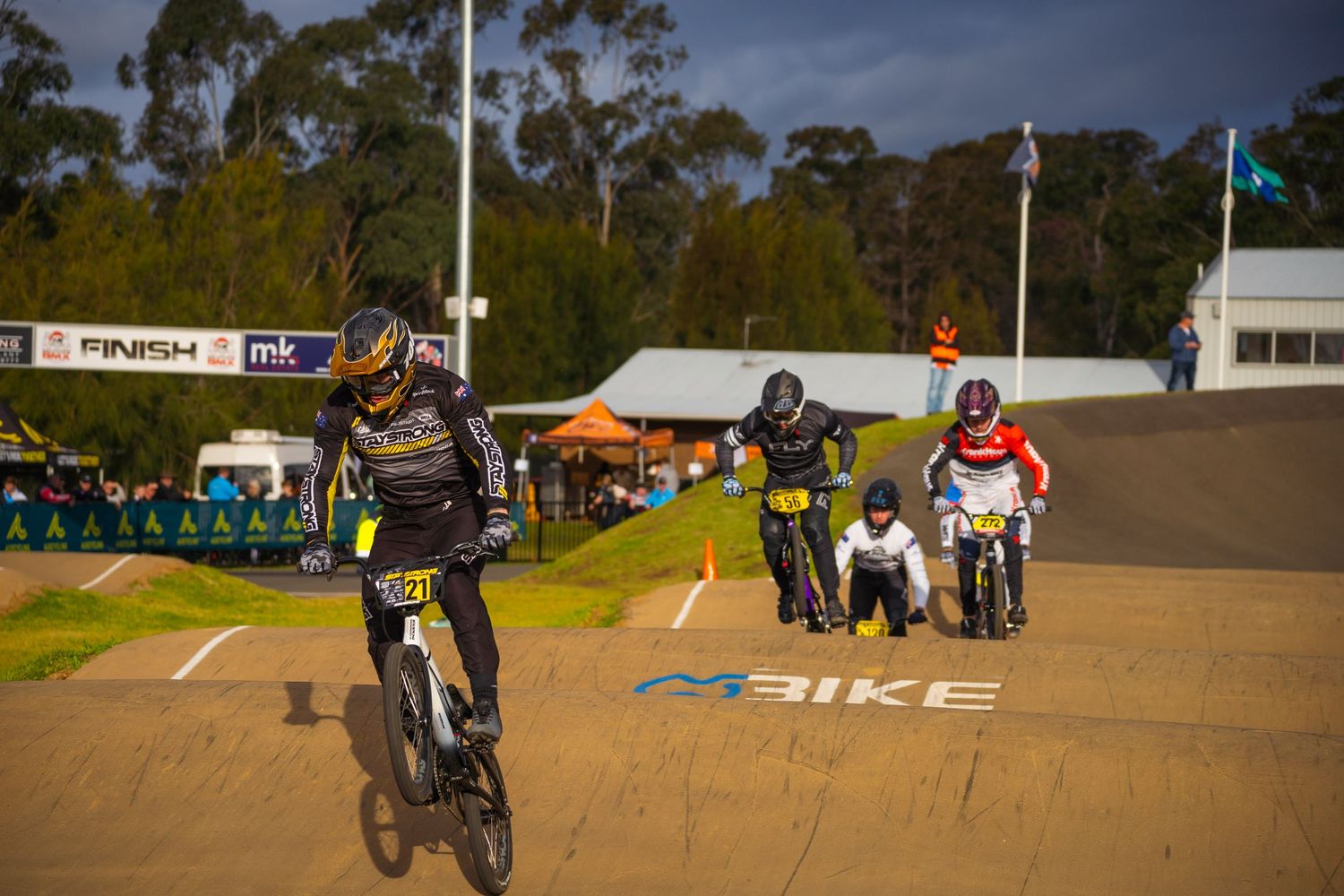 BMX riders racing over dirt jumps on competition track.