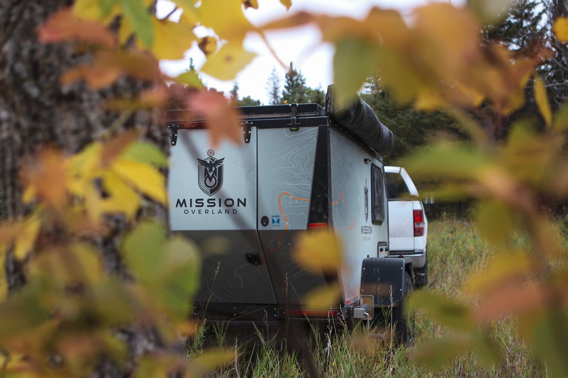 Mission camper van viewed through autumn leaves in an outdoor setting.