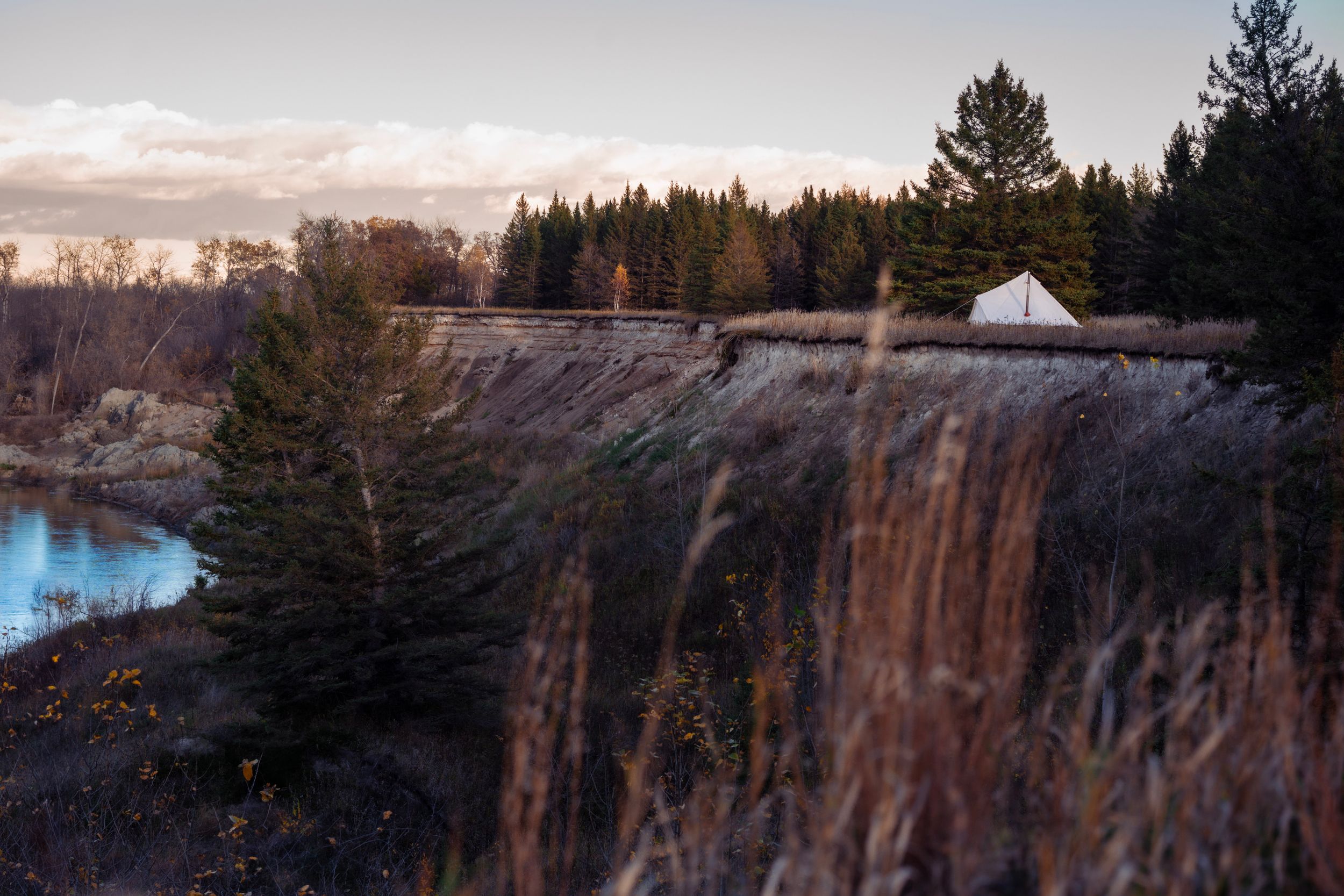 White glamping tent perched on cliff edge overlooking water at dusk.