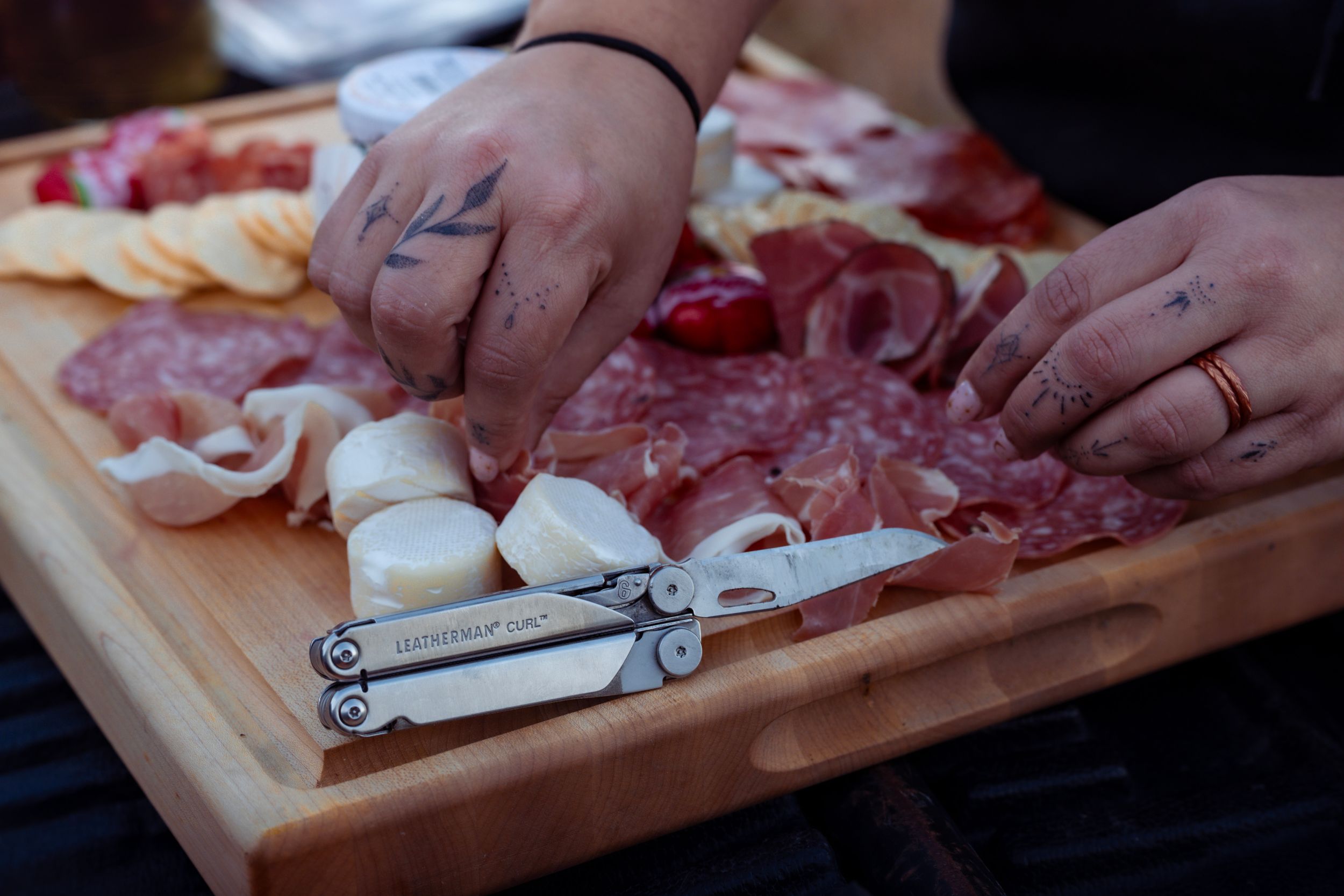 Hands preparing charcuterie board with meats and cheeses on wooden cutting surface.