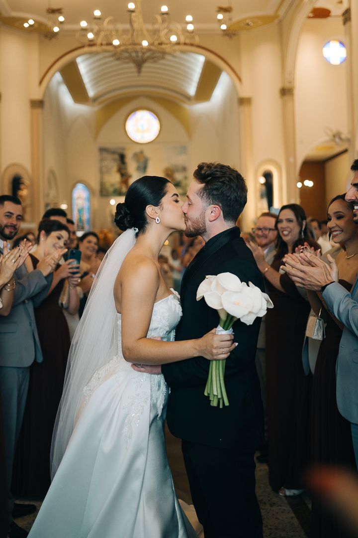 noivos se beijando após cerimônia de casamento na igreja com convidados celebrando ao redor