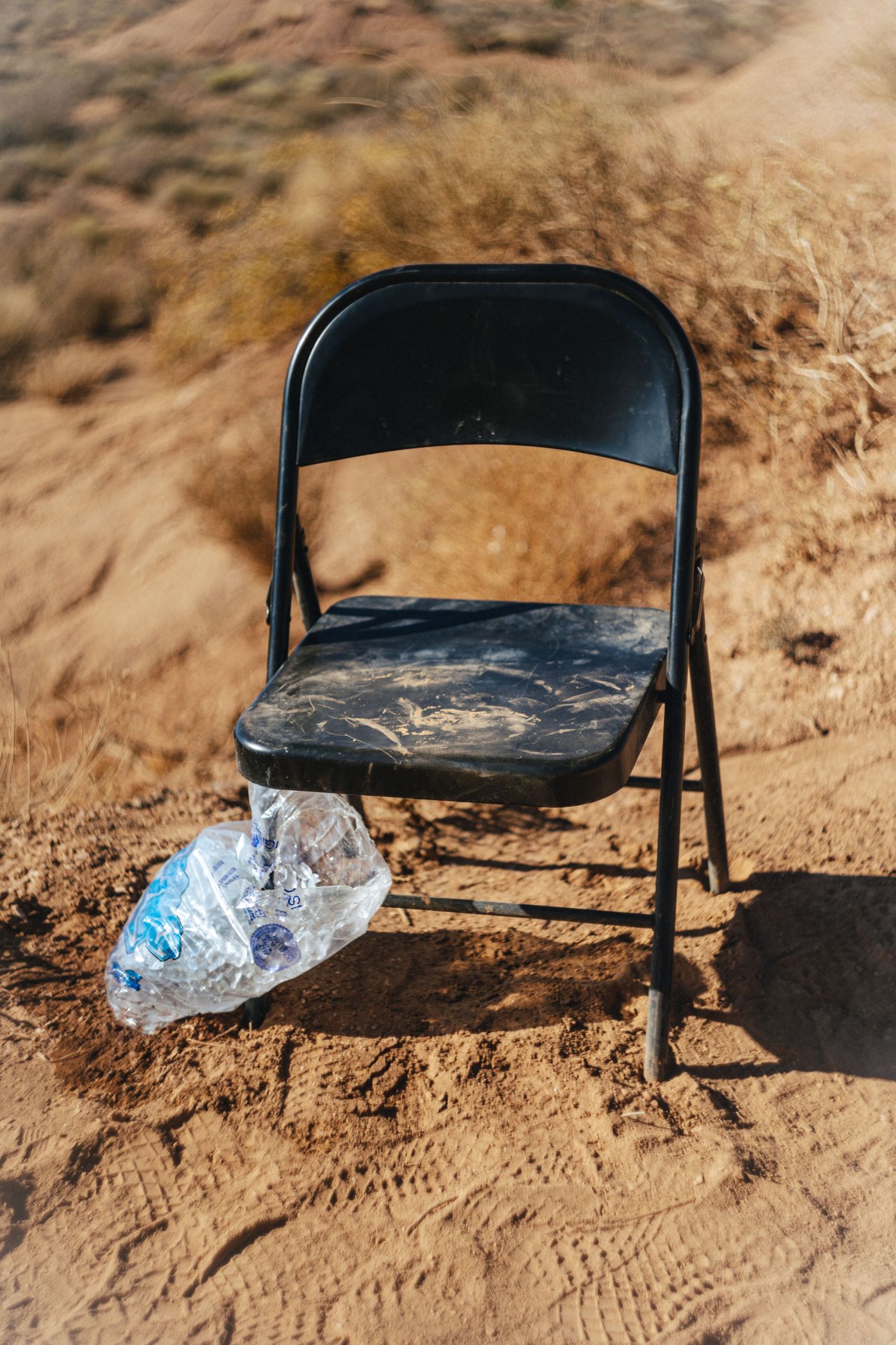 A black folding chair sits on dusty ground with a water bottle beside it.