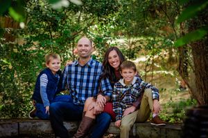 A family wearing coordinated blue and brown outfits sits together on outdoor stone steps for a portrait session.
