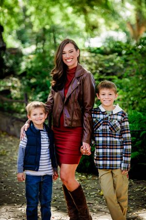 Three people in casual fall attire pose together on a wooded path during an autumn photoshoot.
