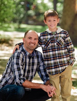 A family group in coordinating plaid shirts poses together on outdoor steps in natural lighting.