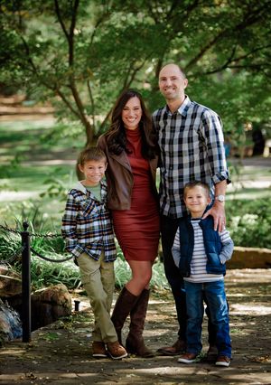 A family poses together in a wooded outdoor setting wearing coordinating plaid and burgundy outfits.
