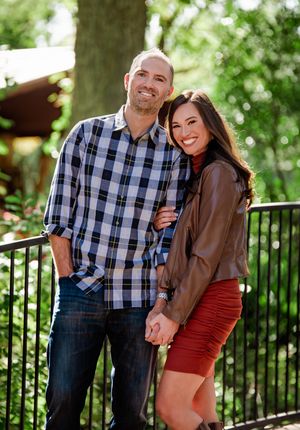 A couple poses together outdoors in a garden setting wearing coordinated outfits of plaid and burgundy.