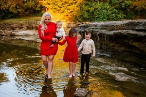 Children splash and play in a shallow creek during golden hour as sunlight filters through autumn trees.