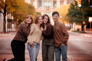 A group of friends in autumn clothing laughing together on a tree-lined street at sunset.