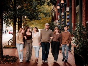A group of friends walk together along a brick sidewalk with autumn trees and lanterns in an urban setting.