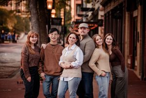 Group of friends in casual fall sweaters and jeans gather together on a brick-lined street at sunset.