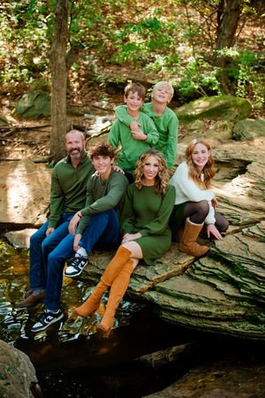 A group wearing matching green shirts sits together on a large rock formation in a wooded outdoor setting.