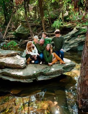 A family relaxes together on rocky outcrops beside a peaceful woodland stream on an autumn day.