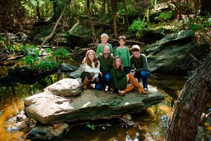 People in casual attire gathered on rocky outcrops near a stream in a forest setting.