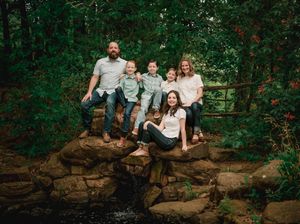 A group sits together on a rustic stone wall surrounded by lush green forest foliage.