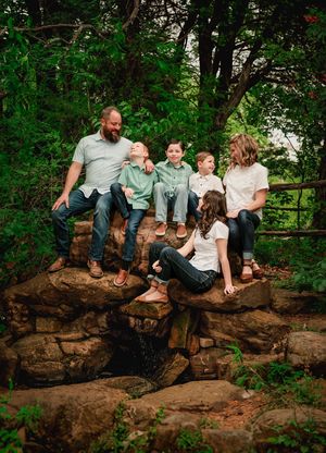 A group sits together on a rocky outcrop surrounded by lush greenery in an outdoor nature setting.
