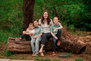 Family members sit together on rustic wooden logs in a lush green forest setting.