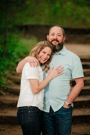 A couple shares tender moments while posing on wooden steps surrounded by lush greenery in a romantic outdoor setting.