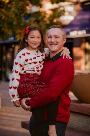 A festive holiday portrait showing matching red and white outfits with hearts and plaid patterns in an outdoor setting.